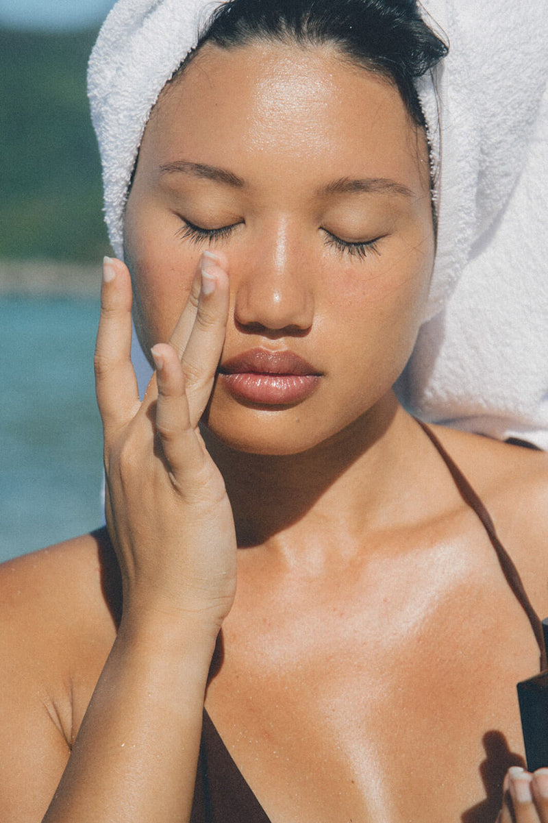 Woman with a towel wrapped around her hair is applying a face serum.