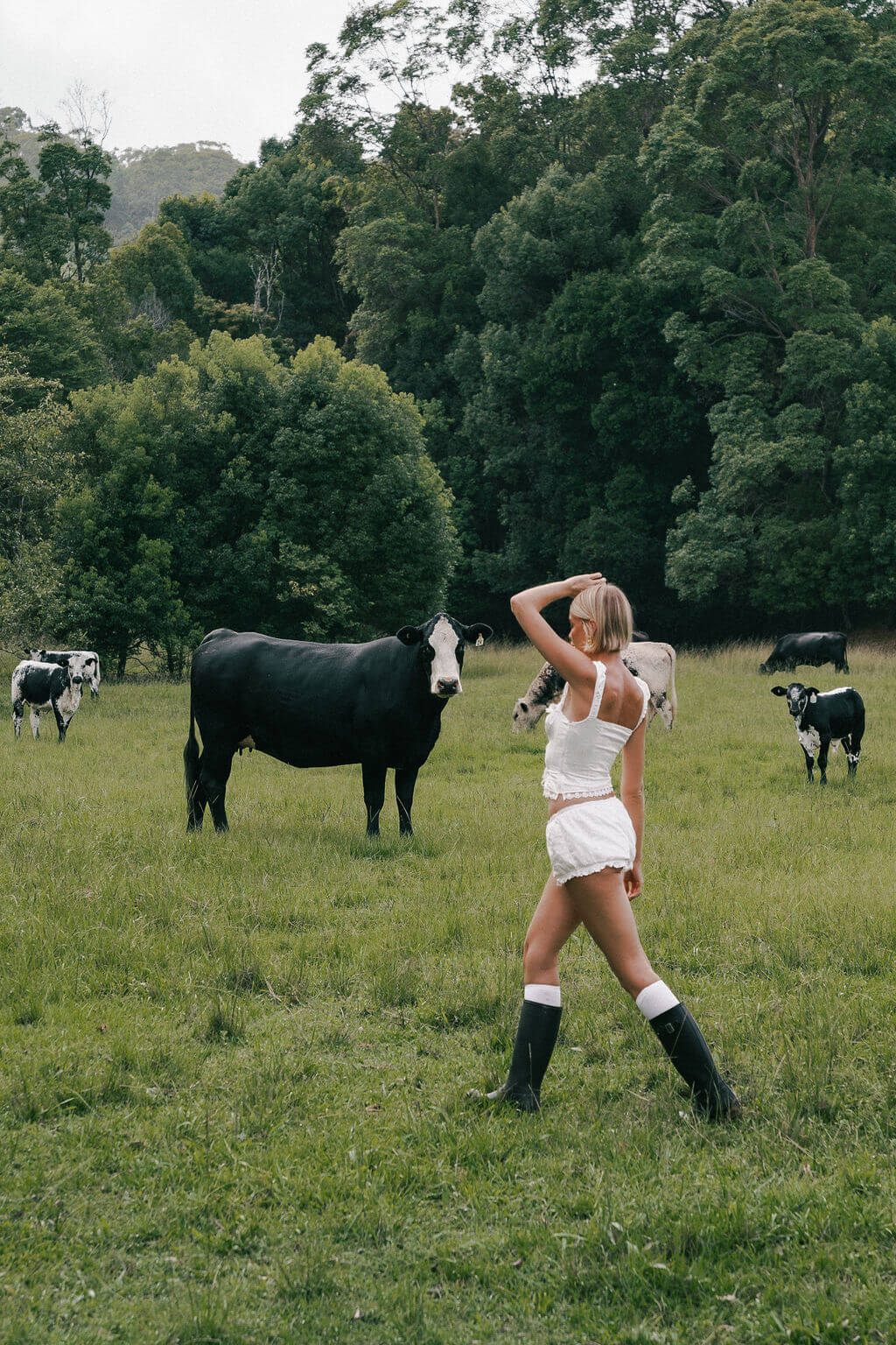 A woman walking on a grass field with cows.