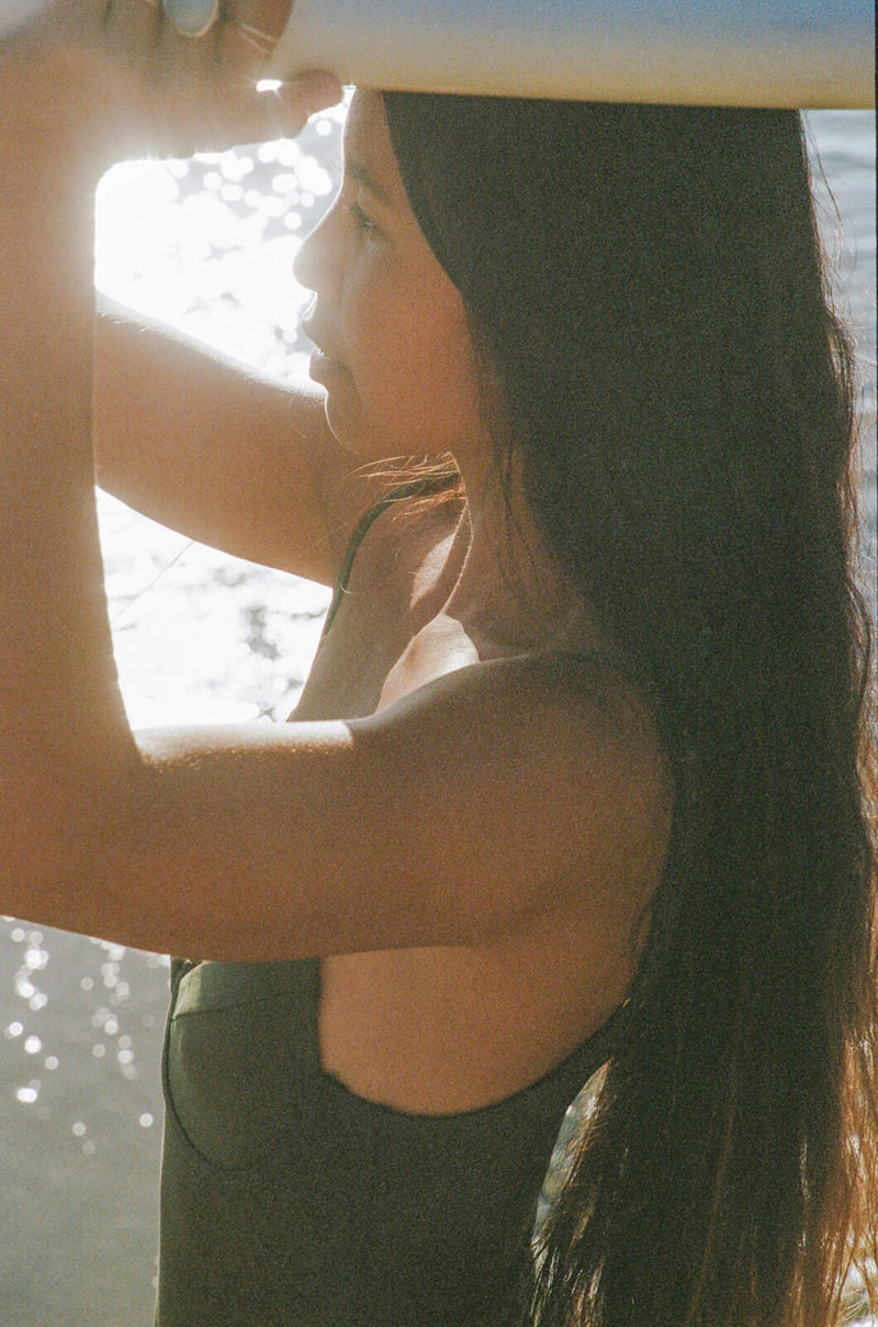 Woman wearing a bathing suit is carrying a surfboard on her head.